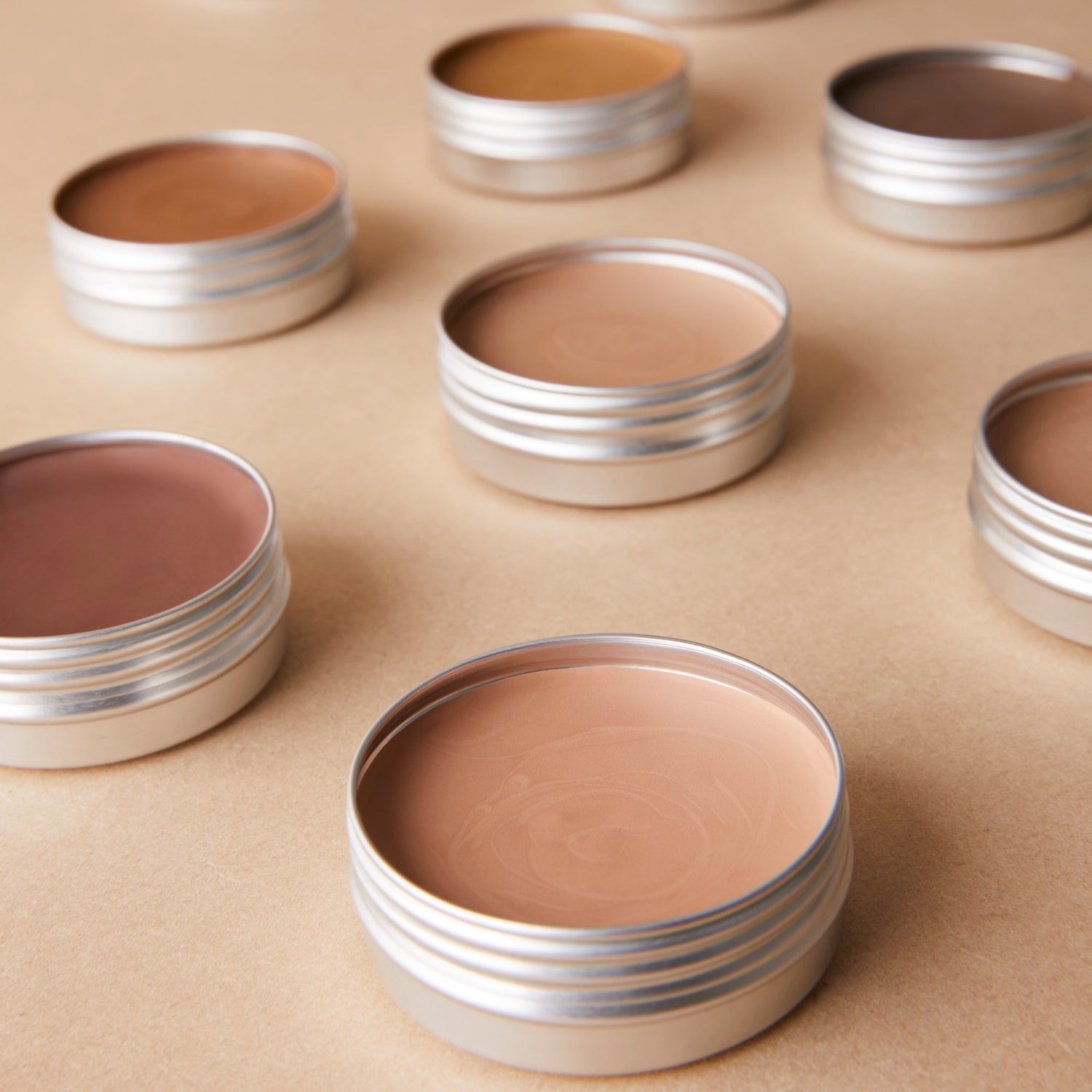 Different coloured round tins of foundation on light brown background 