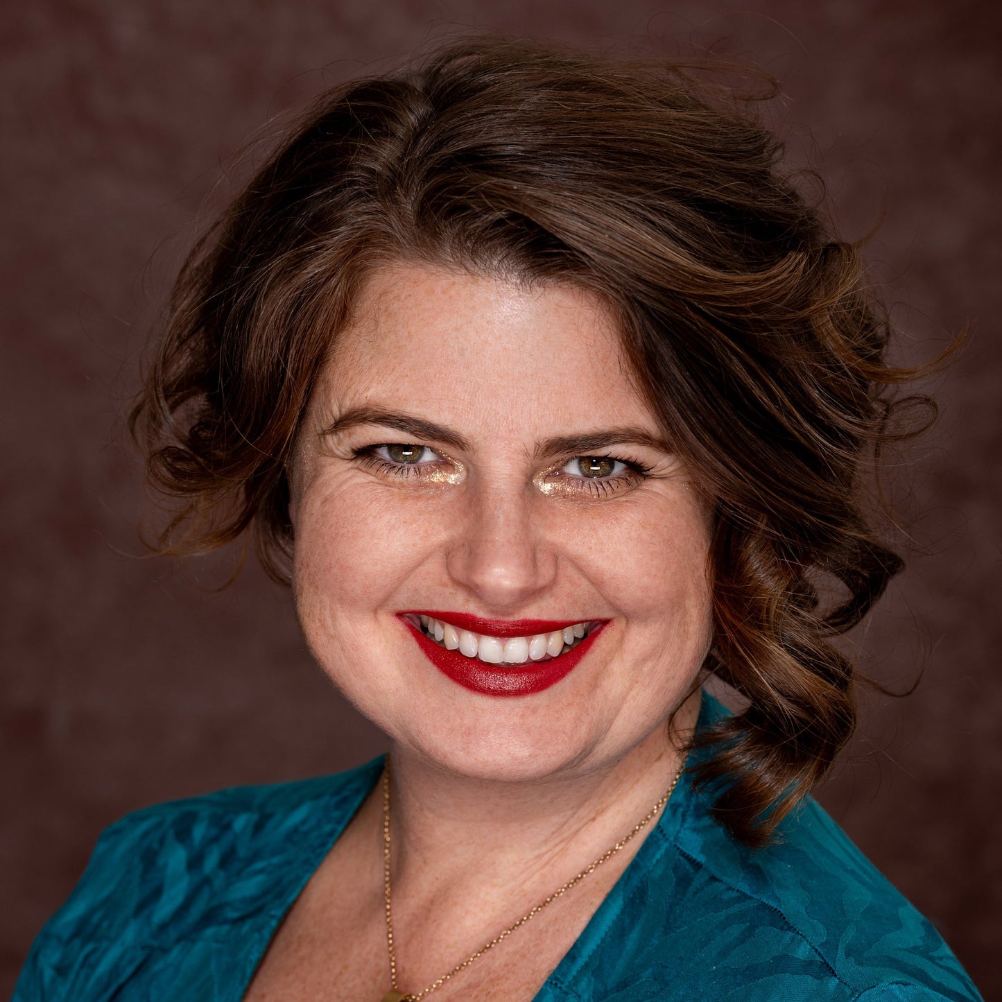 brunet in blue dress on brown background brick red lipstick and gold shimmer around eyes