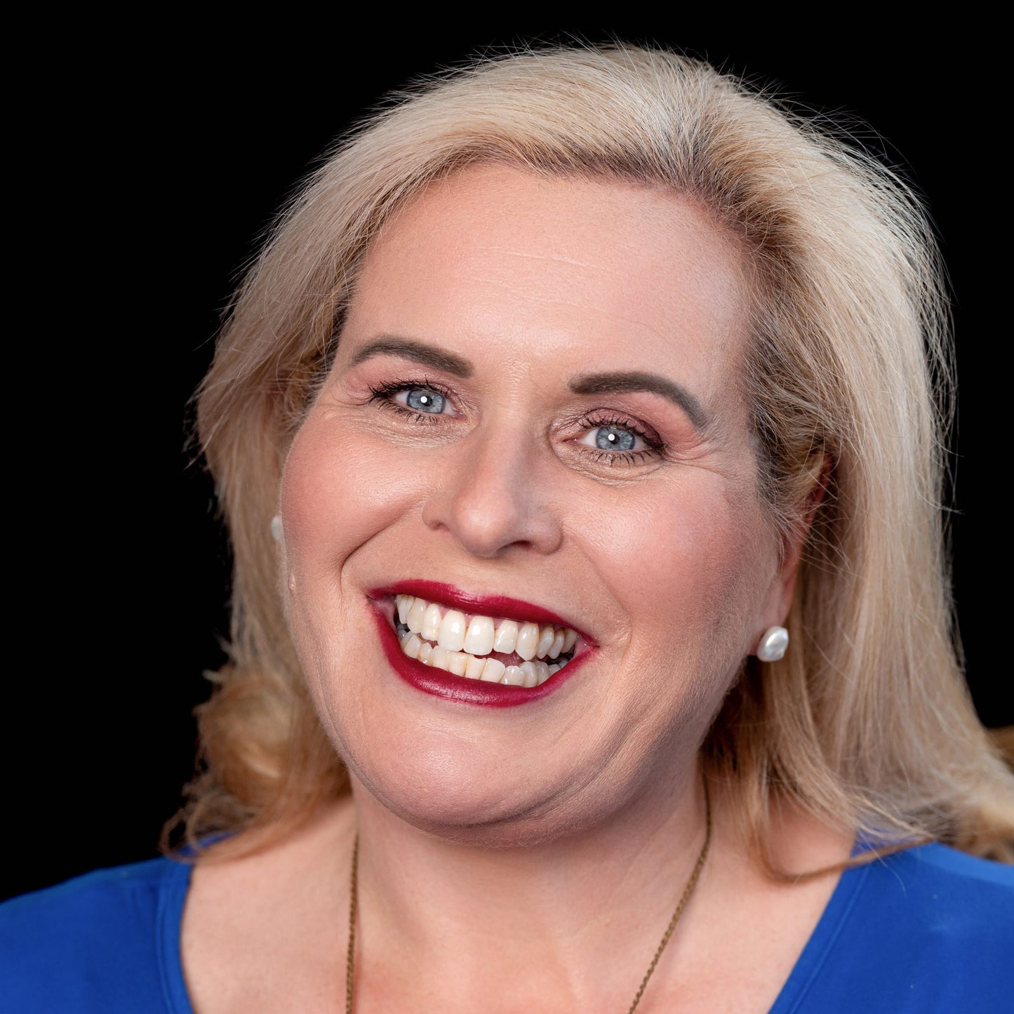 blond woman with bright blue eyes on black background wearing ravishing foundation and tango lipstick