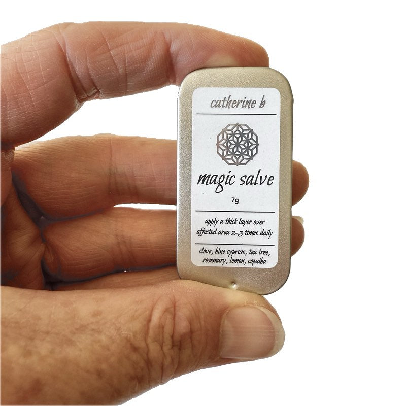 Hand holding a small container labeled 'magic salve' with a white label.