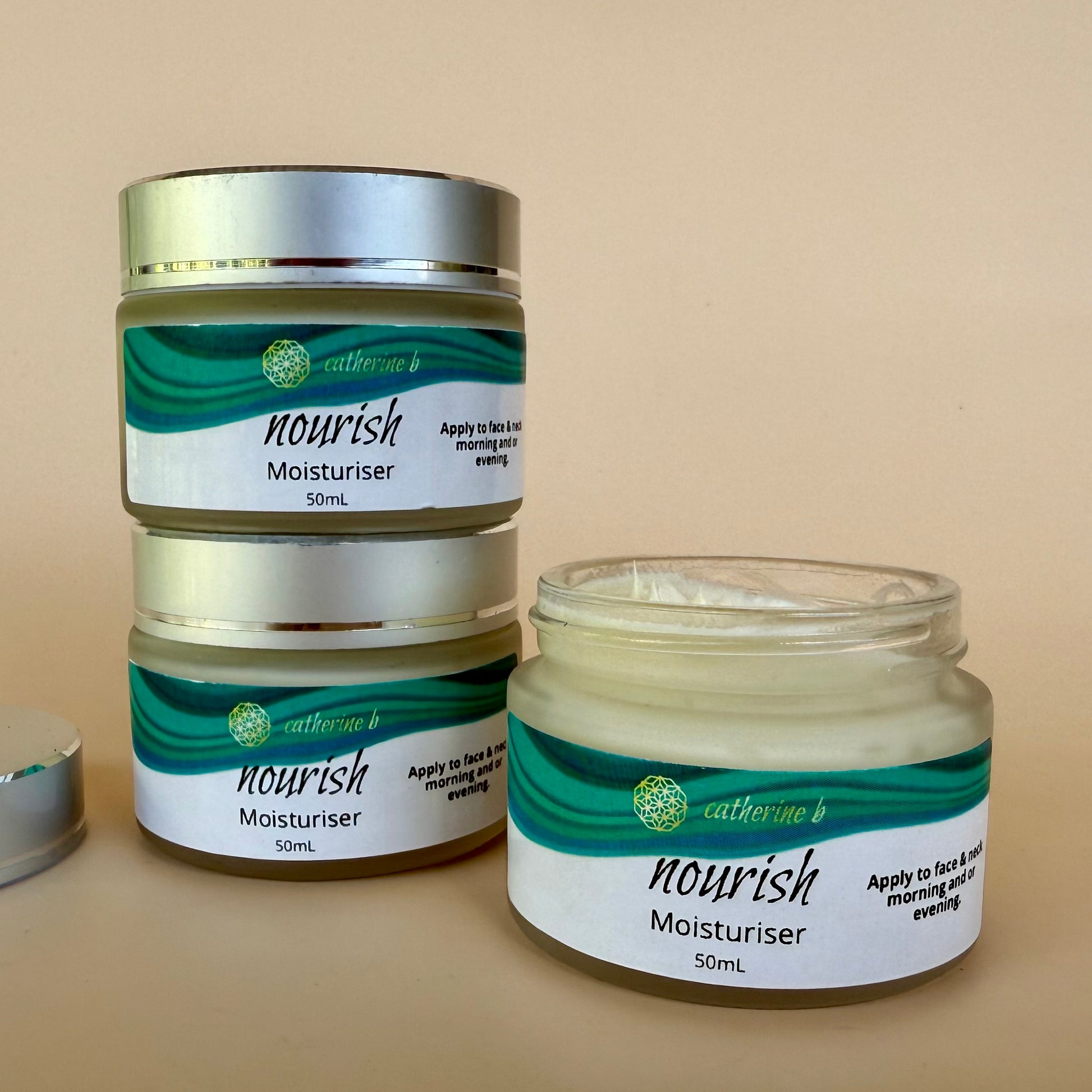Three jars of 'nourish' moisturizer with green and white labels on a beige background